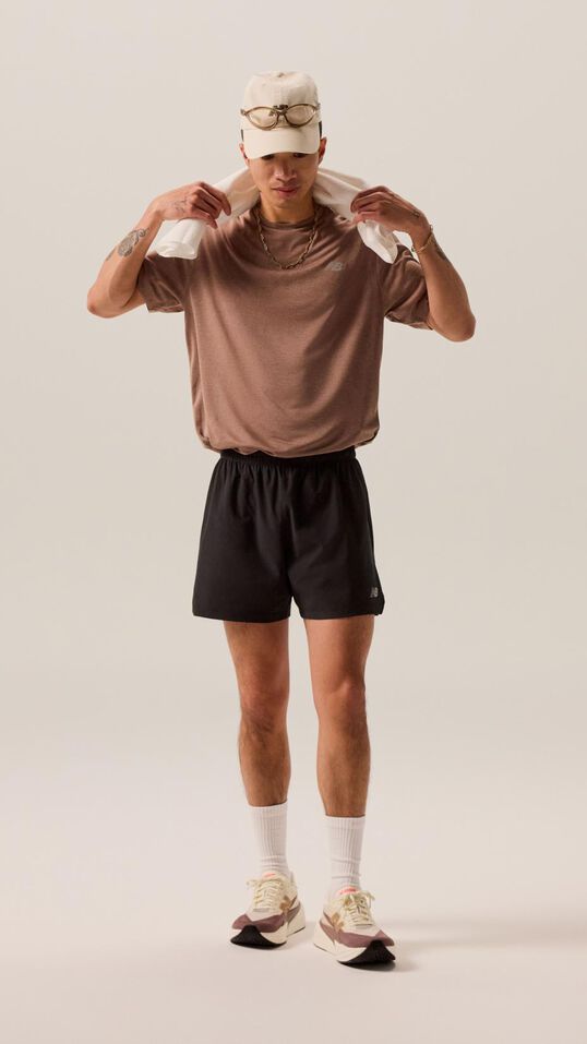 A man wearing black shorts and maroon shirt while holding a towel over his head. 