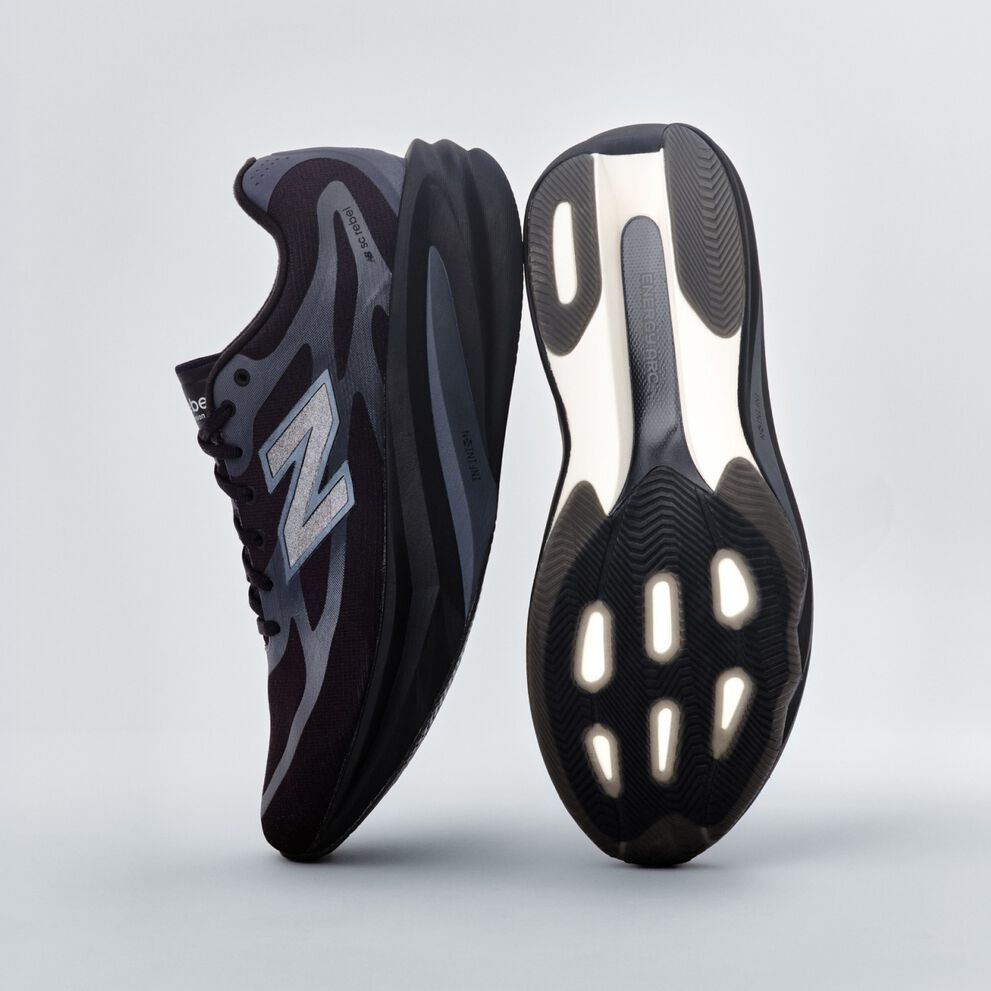 A pair of black New Balance sneakers sitting on a gray studio backdrop. 