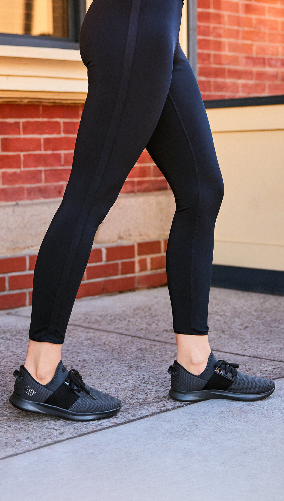 Waist down shot of a woman standing on the sidewalk wearing leggings and black Nergize shoes. 