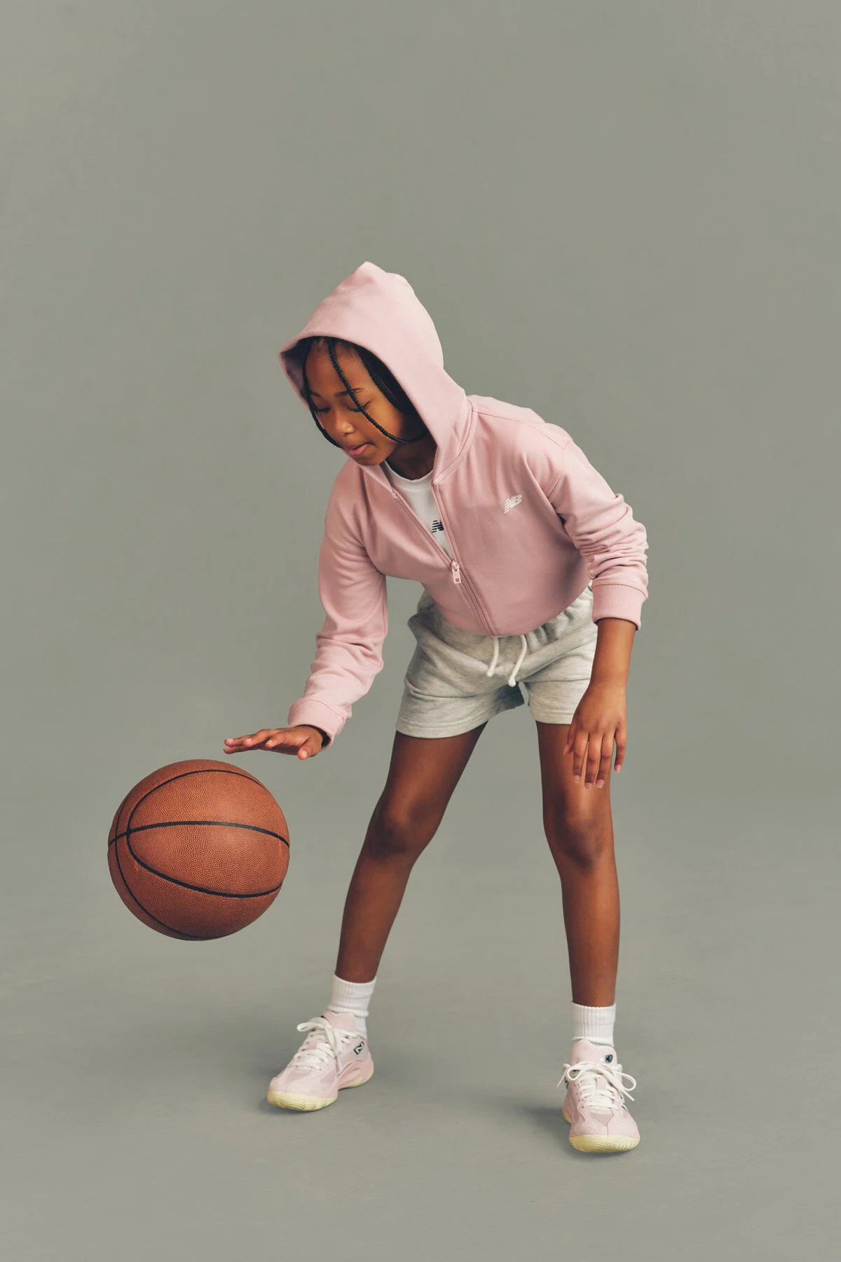 Kid playing with a basketball against a grey studio background.