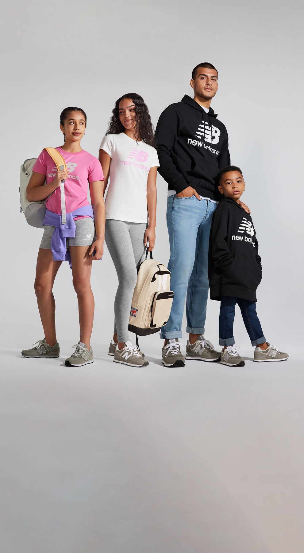 A young family of four wearing various NB Essentials tops with matching grey NB Classic 574 sneakers as they pose in front of a light grey studio backdrop 