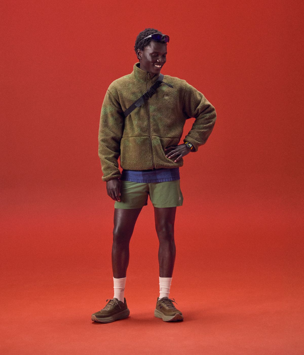 Young man in a green outfit smiling on a red background.