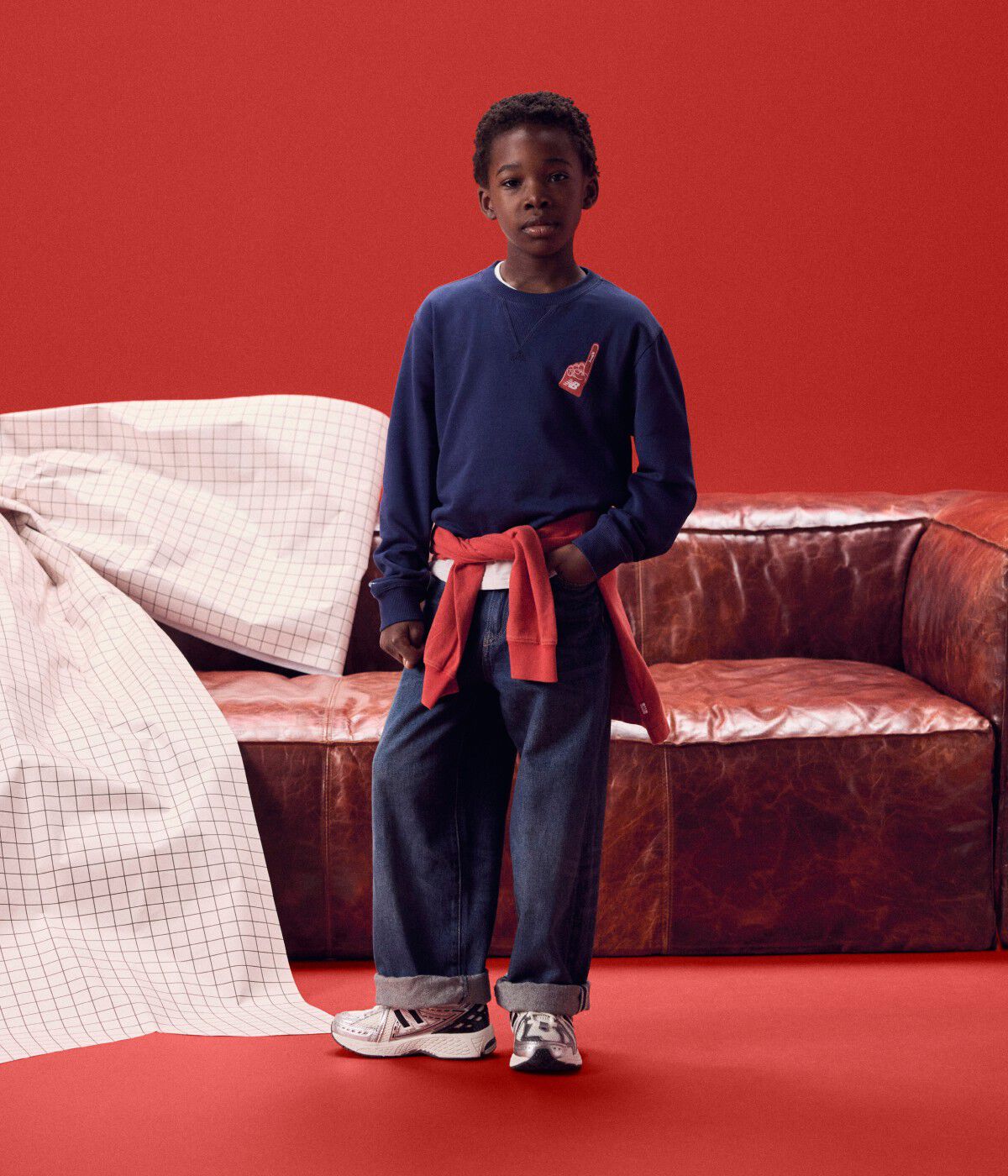 Niño con una camisa de manga larga azul marino frente a un sofá rojo.