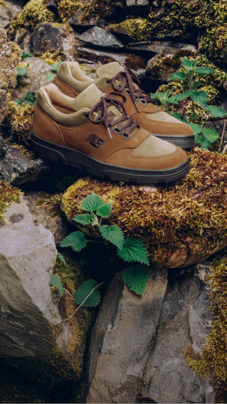 Un par de zapatillas New Balance Made in UK colocadas en un jard&iacute;n de rocas cubierto de musgo, rodeadas de peque&ntilde;as plantas verdes.
