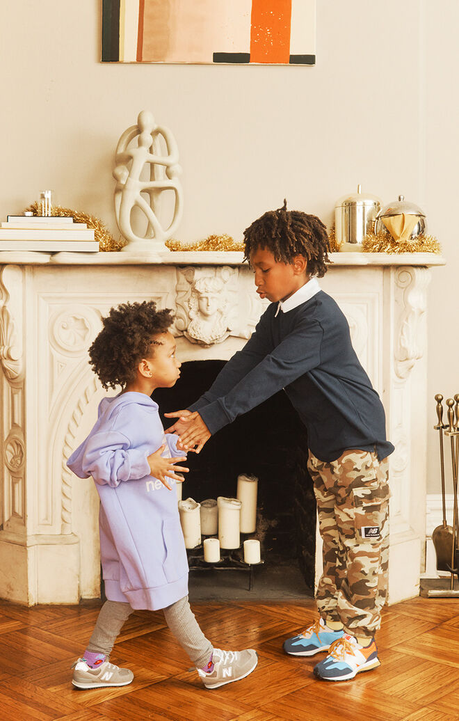 Two kids wearing New Balance clothing and shoes posed against a decorative fireplace