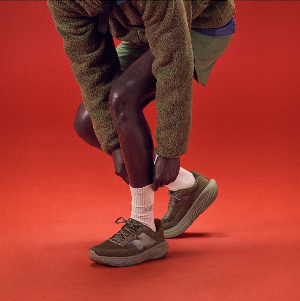 Joven inclinándose para atarse los zapatos sobre un fondo rojo.