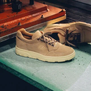 Knee down view of a woman wearing a pair of New Balance Made in UK sneakers standing in a beige studio environment.