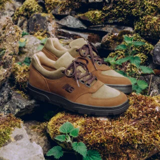A pair of New Balance Made in UK sneakers sitting in a moss covered rock garden surrounded by small green plants.