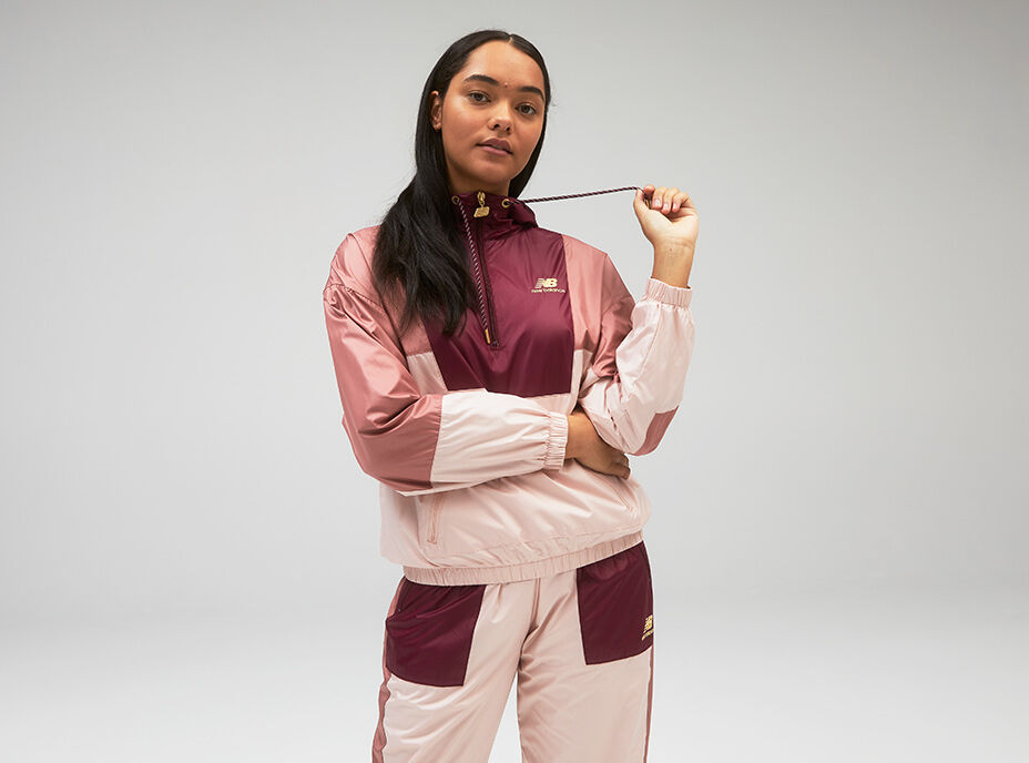 Young woman wearing pink and maroon track jacket while tugging on one of the hoodie strings.