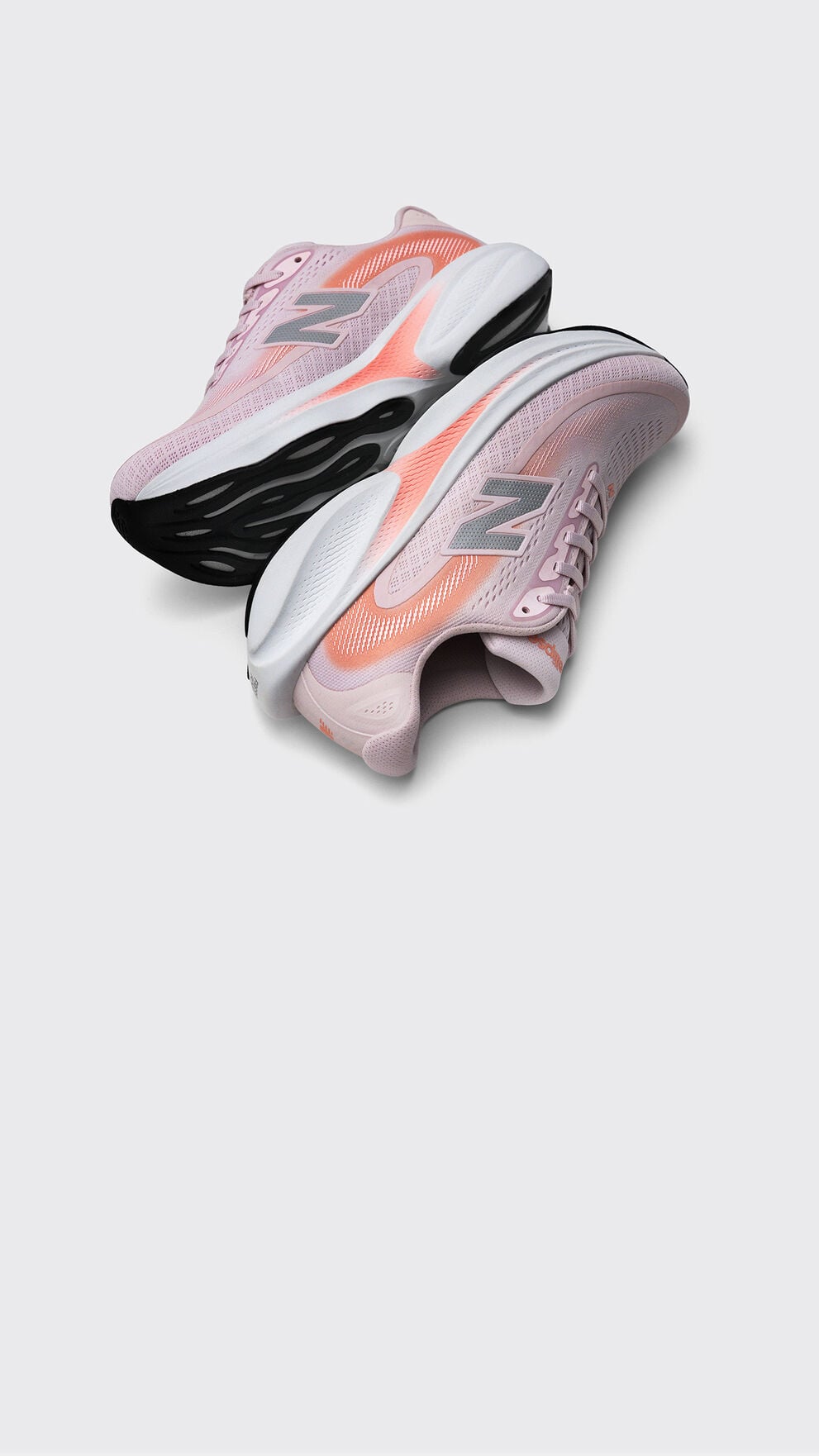 Pair of light pink New Balance running shoes with coral accents and chunky black-and-white soles displayed on a light gray background. 
