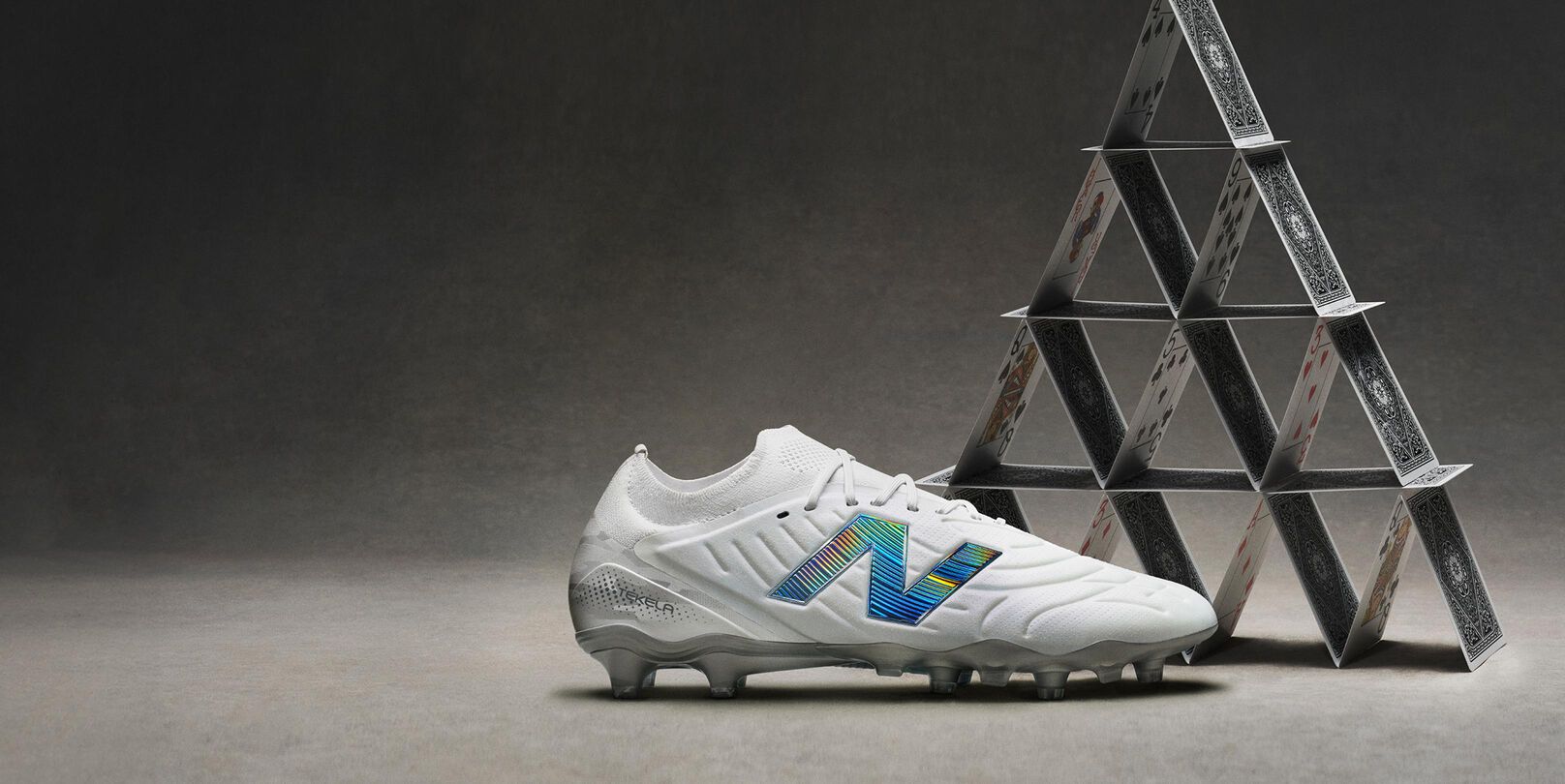 Side profile shot of white cleats with blue accents placed in front of a pyramid of cards.