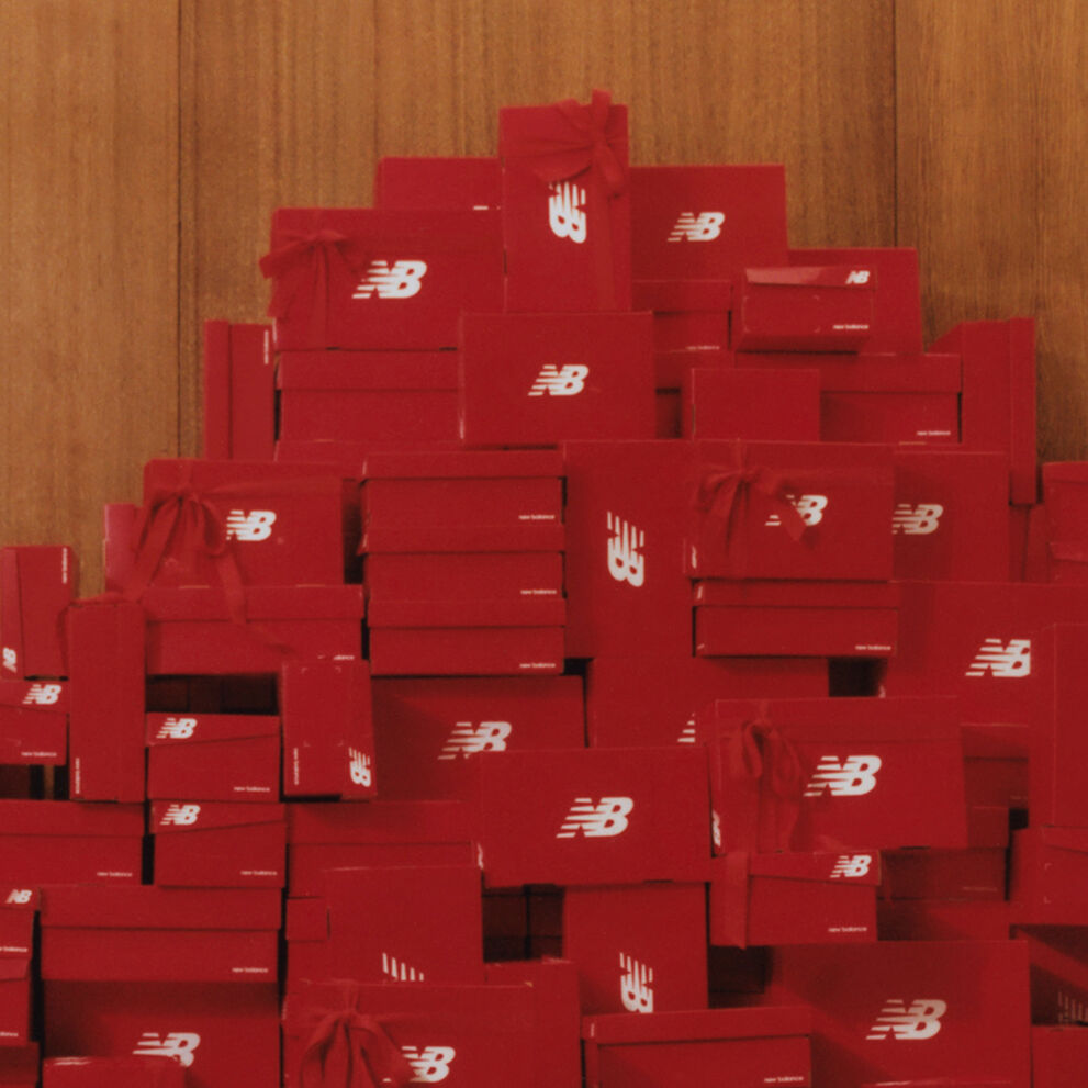 A large stack of red New Balance shoe boxes with red bows attached piled high against a wood panel wall