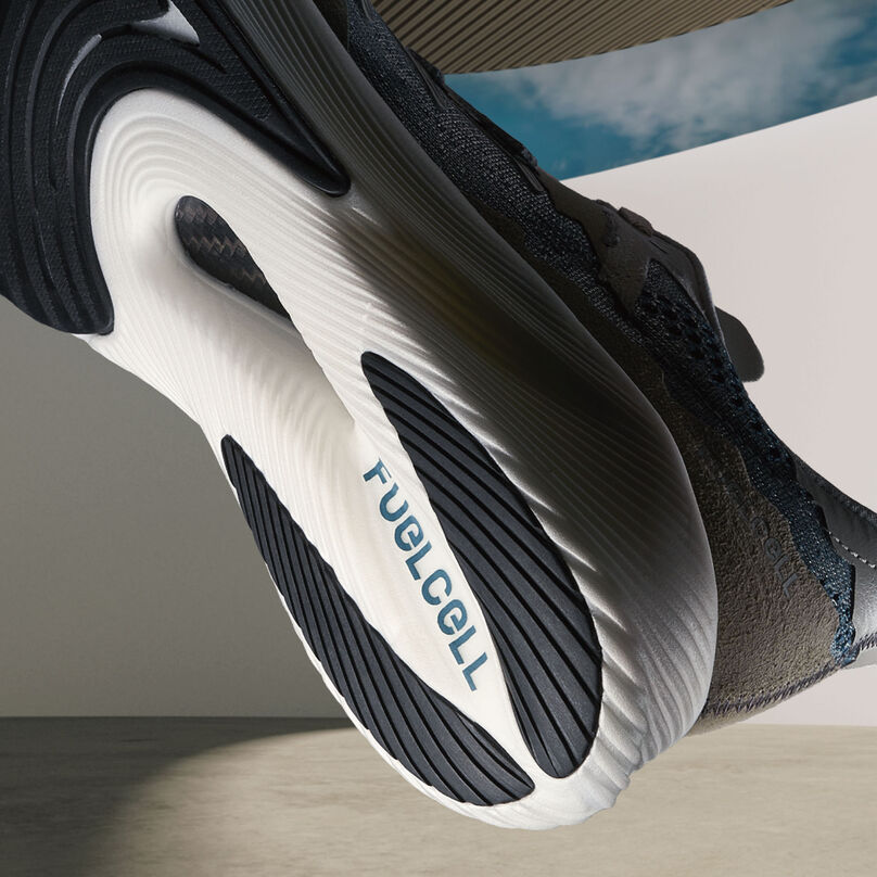 The heel of a steel grey NB x Tokyo Design Studio RC Elite running shoe floating in space in front of a 3D rendered architectural background and blue sky
