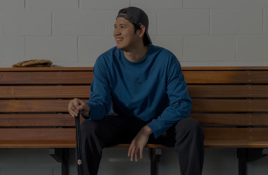 Shoehei Ohtani sitting in a locker room in a blue jacket. 