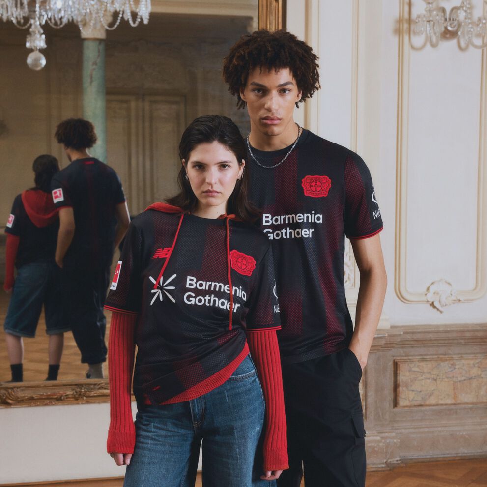 Young couple wearing a black soccer jersey in front of a mirror.  