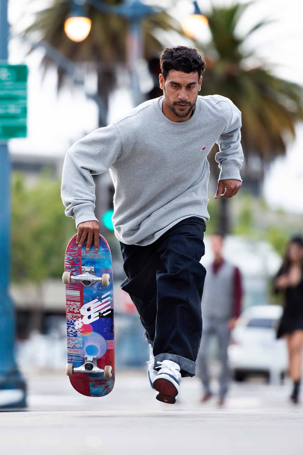 Tiago Lemos running and holding a skateboard in one hand.