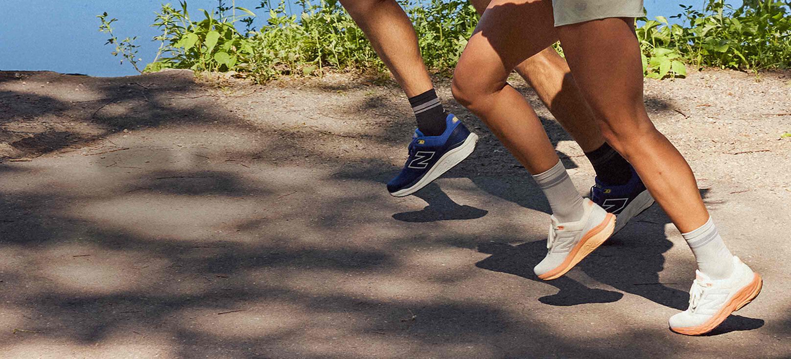 Two people wearing New Balance footwear and apparel running in a park. 