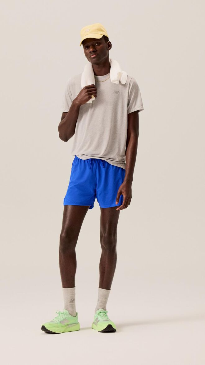 A runner in a grey shirt and blue shorts with neon green shoes. 