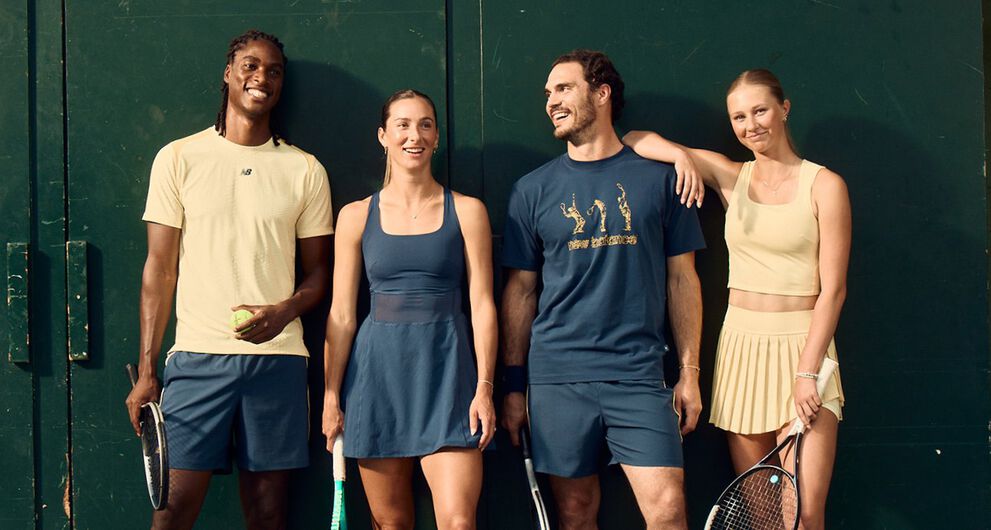 Four tennis players in coordinated athletic apparel stand against a dark green court wall holding rackets and a tennis ball.