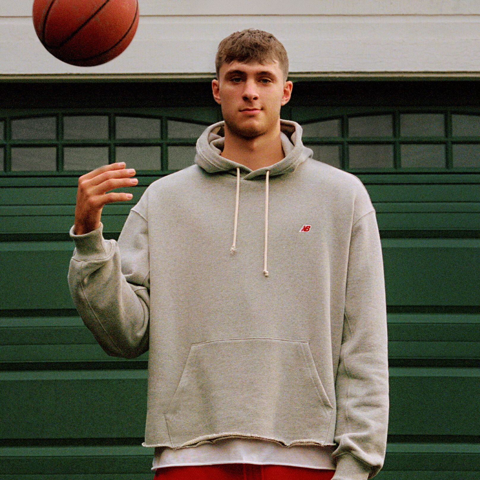 Cooper Flagg, looking at the camera, wearing New Balance apparel, tossing a basketball into the air.