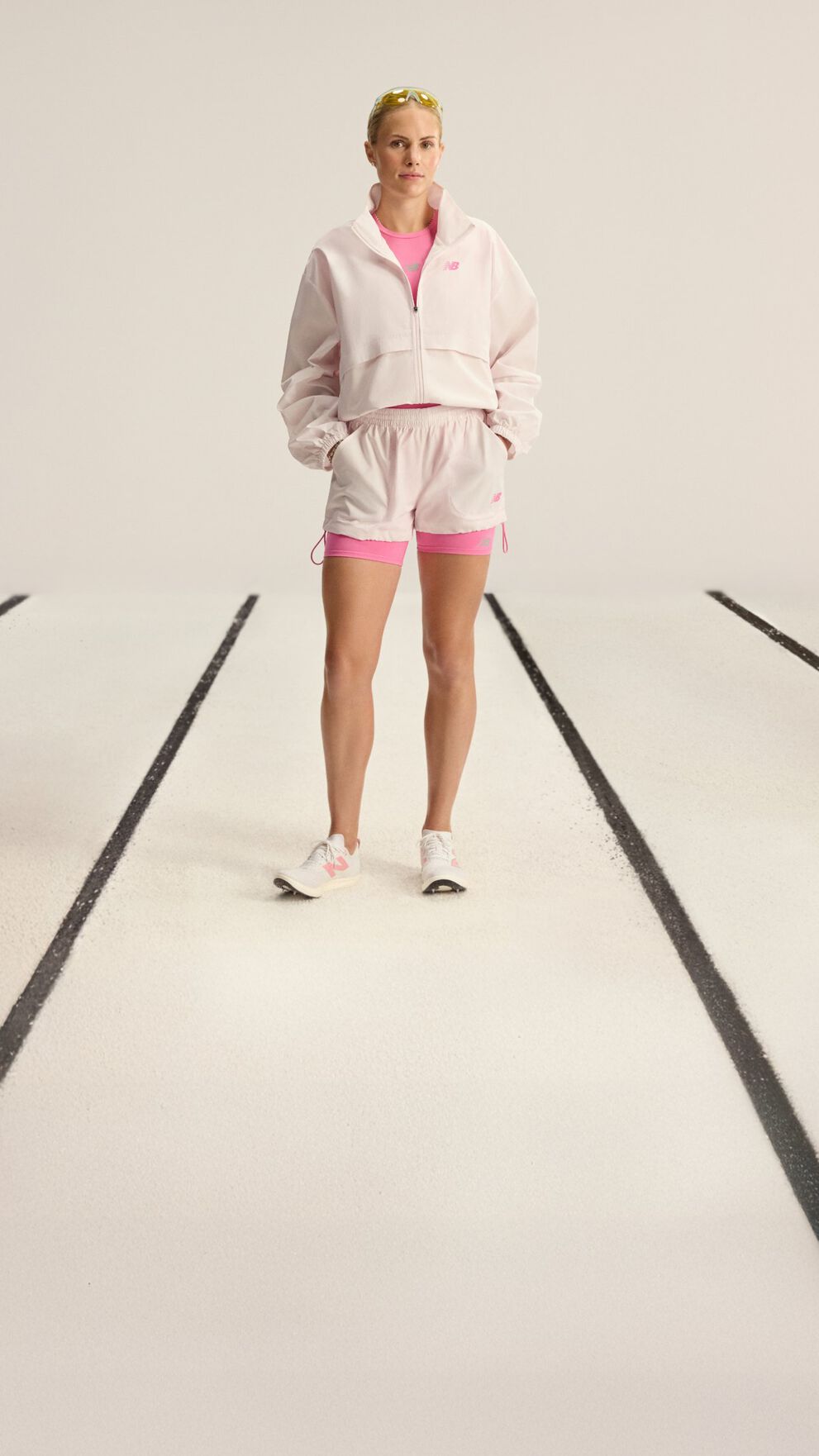 A person is standing on a white surface with black parallel lines, wearing a light pink cropped zip-up hoodie, matching light pink athletic shorts, and a bright pink undershirt.
