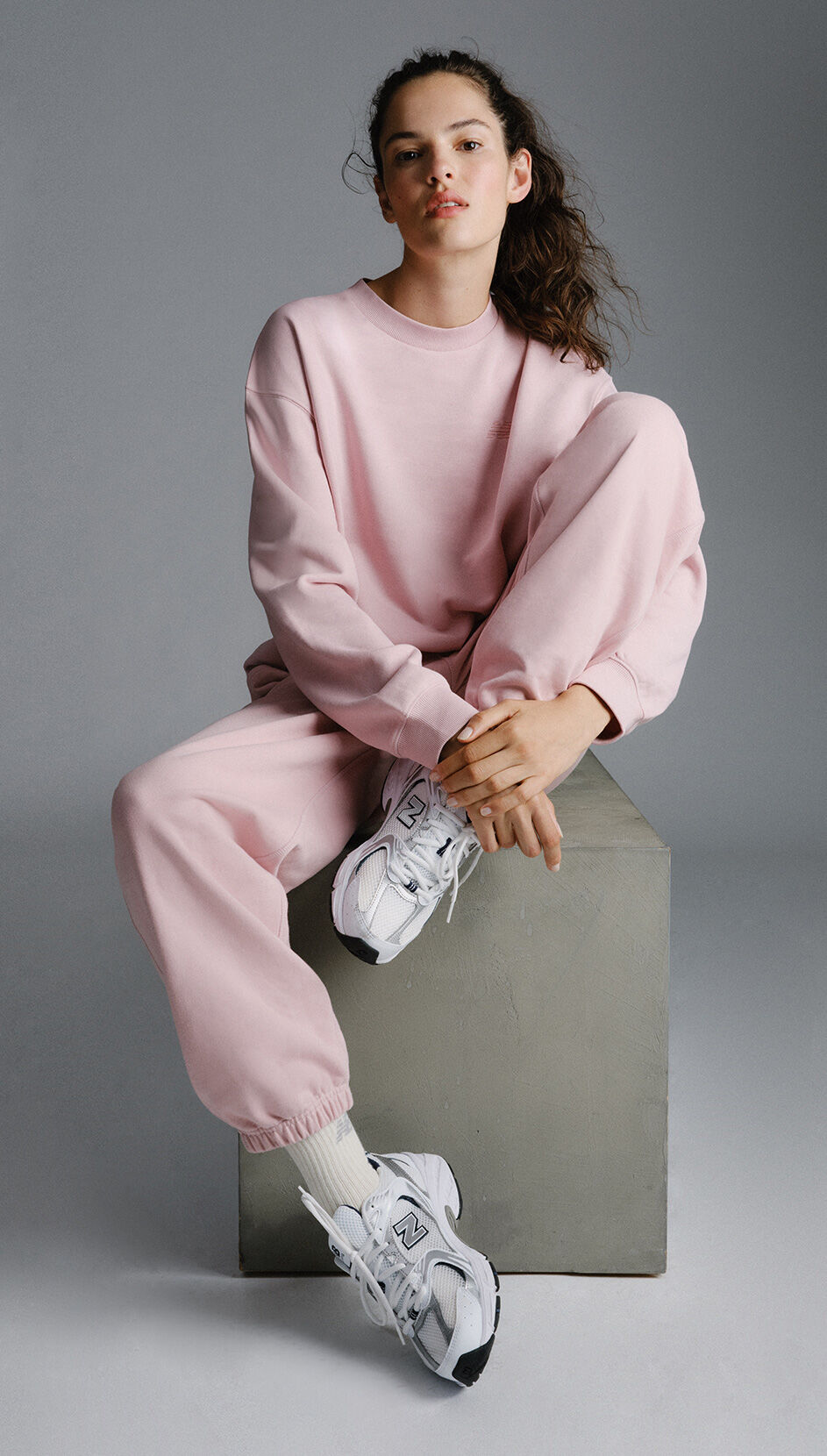 An individual sitting on a box while wearing a pink sweatsuit. 