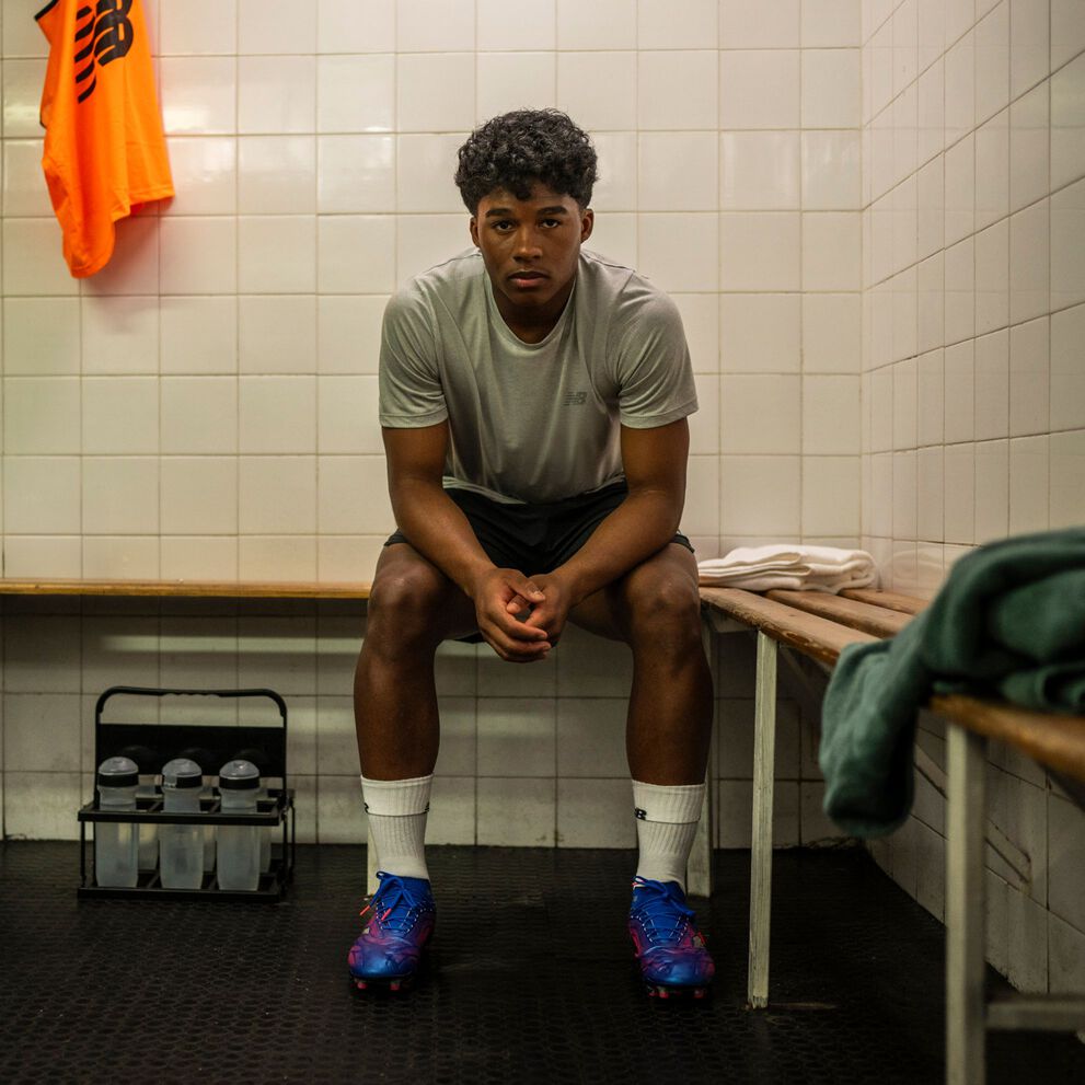Endrick sitting in a locker room, wearing New Balance Tekela soccer cleats.   