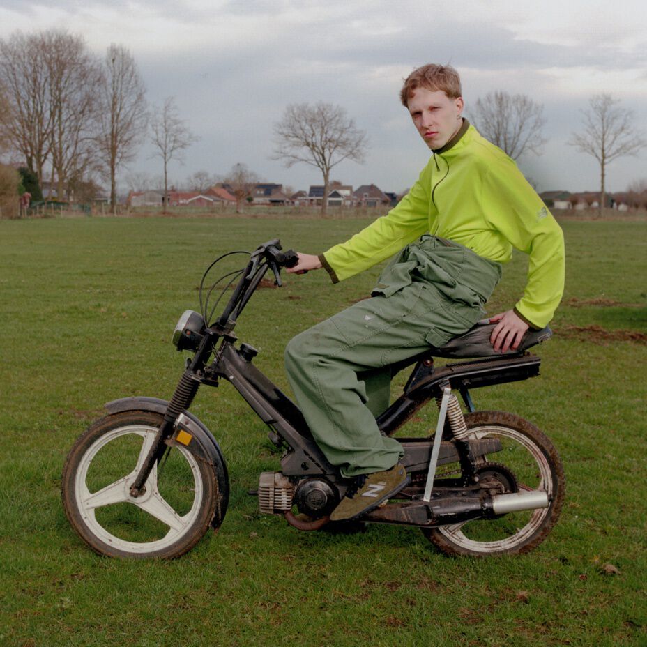 Guy with a green jacket sitting on an old motorcycle.