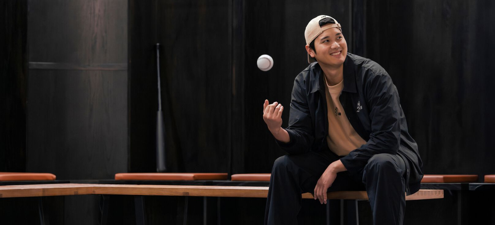 Ohtani sentado en un vestuario lanzando una pelota al aire.  