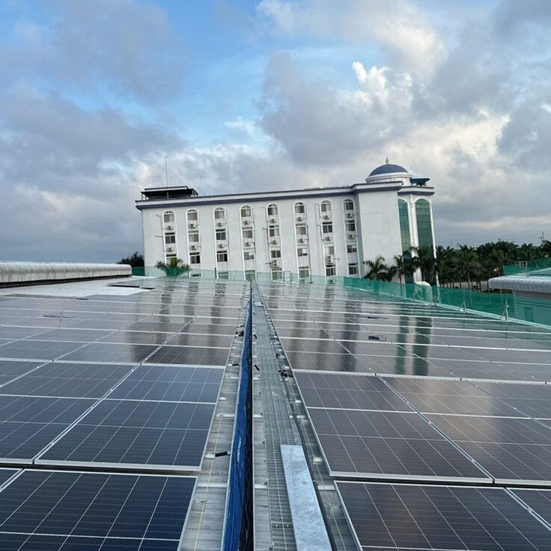 Solar panels set against a building and blue sky with clouds
