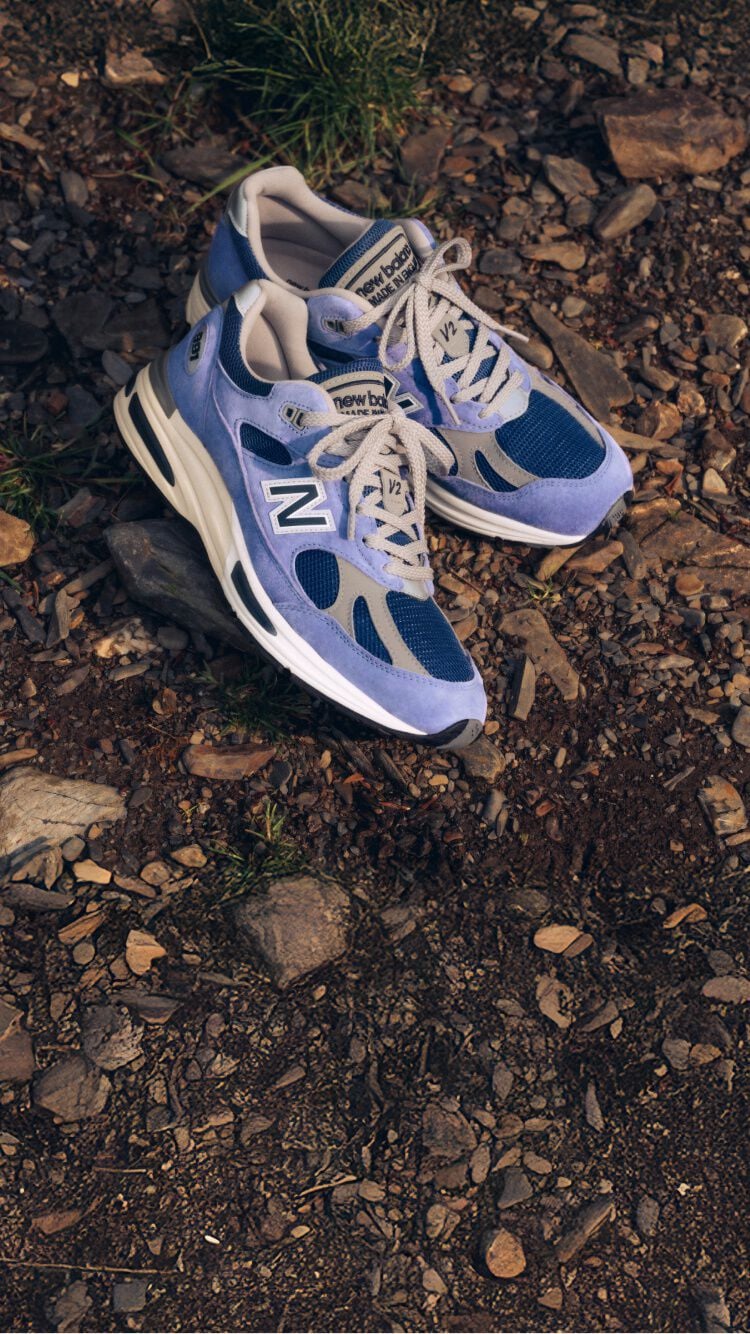 A pair of New Balance Made in UK sneakers on a raw earth surface of dirt and stones.