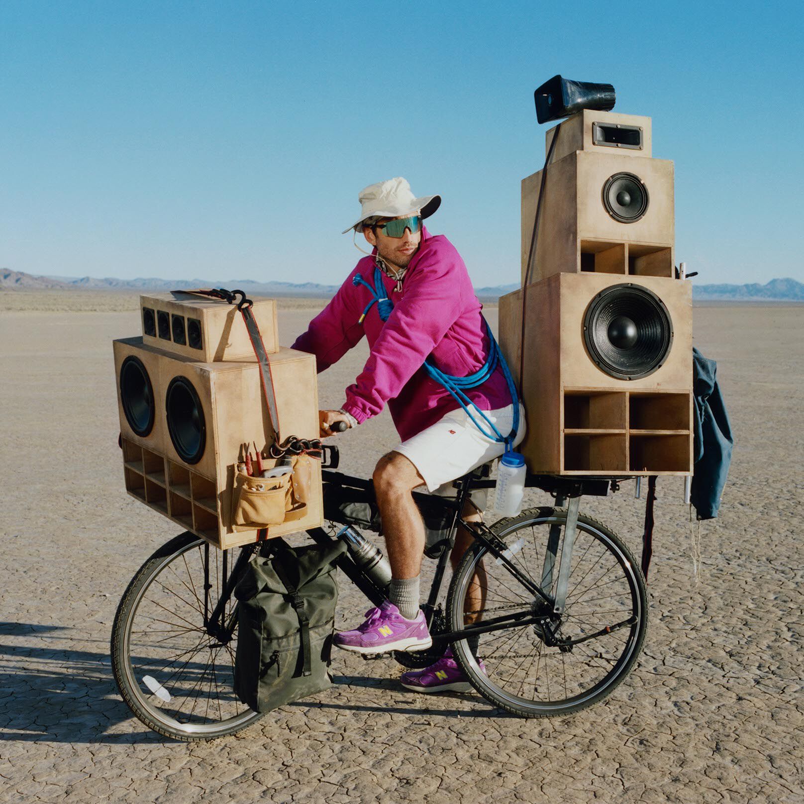 Guy on a bike with giant speakers attached to it wearing a purple sweater and shoes.