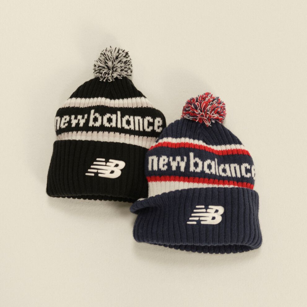 Two New Balance knit pom beanies in black-and-white and navy-red-and-white displayed against a clean neutral background.