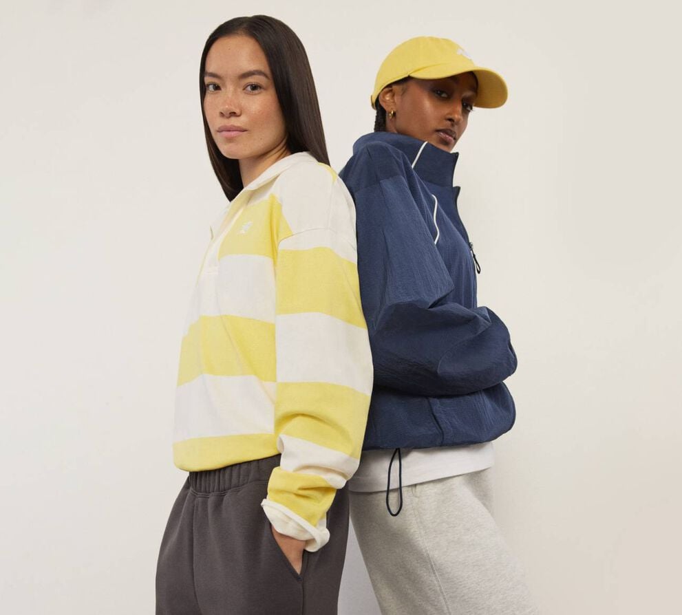 Two woman standing back to back and looking at the viewer.