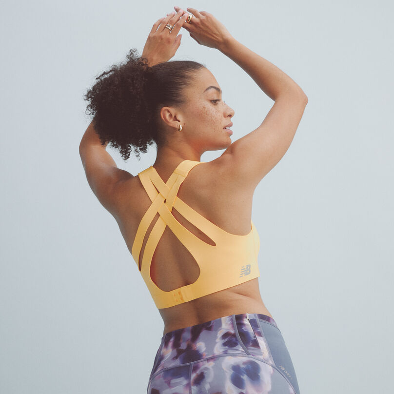 Back view of a woman wearing a yellow NB Fortiflow Bra with multi-colored leggings
