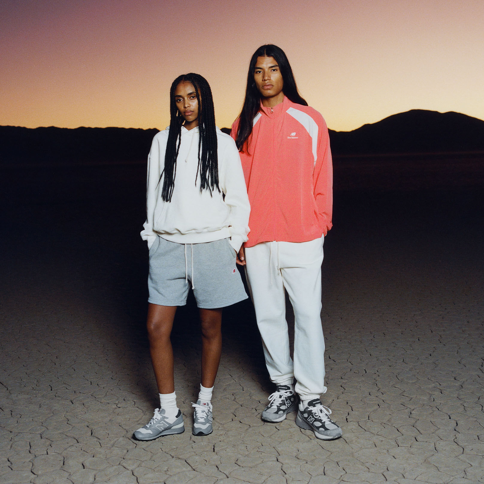 Two people with their hands in their pockets. One is wearing an orange jacket, the other is wearing a white hoodie. 