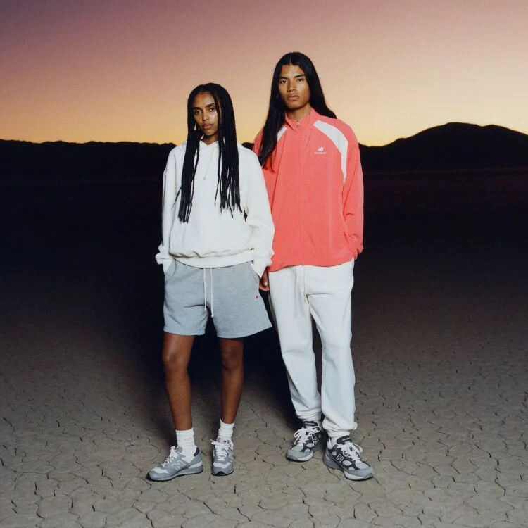 Two people with their hands in their pockets. One is wearing an orange jacket, the other is wearing a white hoodie. 