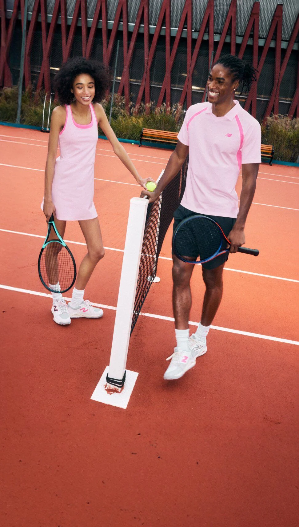 People standing at a tennis net on a clay court, wearing pink tennis apparel and sneakers, holding racquets.