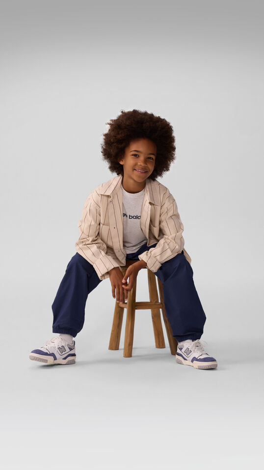 Young kid sitting on a stool wearing blue pants. 