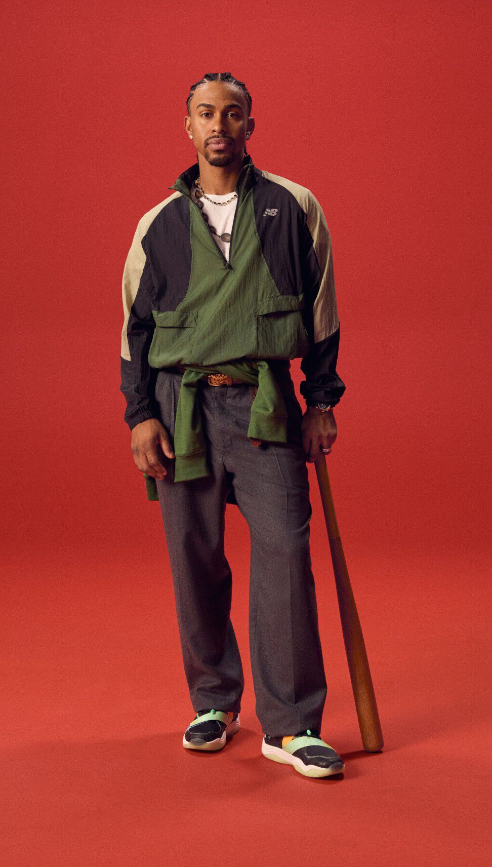 Atleta de béisbol sosteniendo un bate mientras está de pie sobre un fondo rojo.