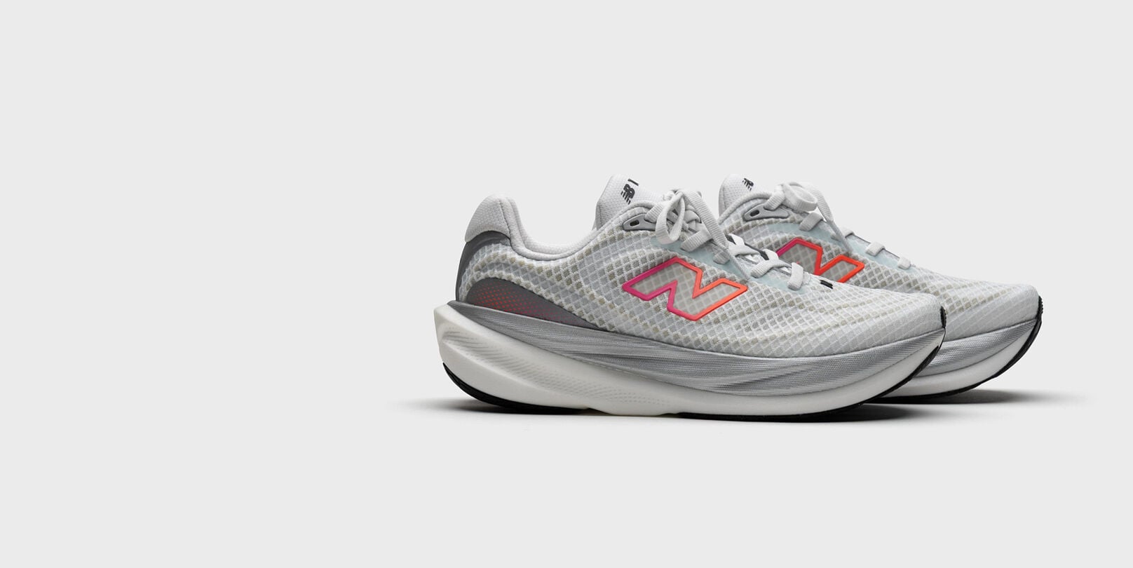 Pair of light gray New Balance running shoes shown in side profile on a neutral background, featuring a translucent mesh upper, thick cushioned midsole, and pink‑to‑orange gradient &ldquo;N&rdquo; logos.