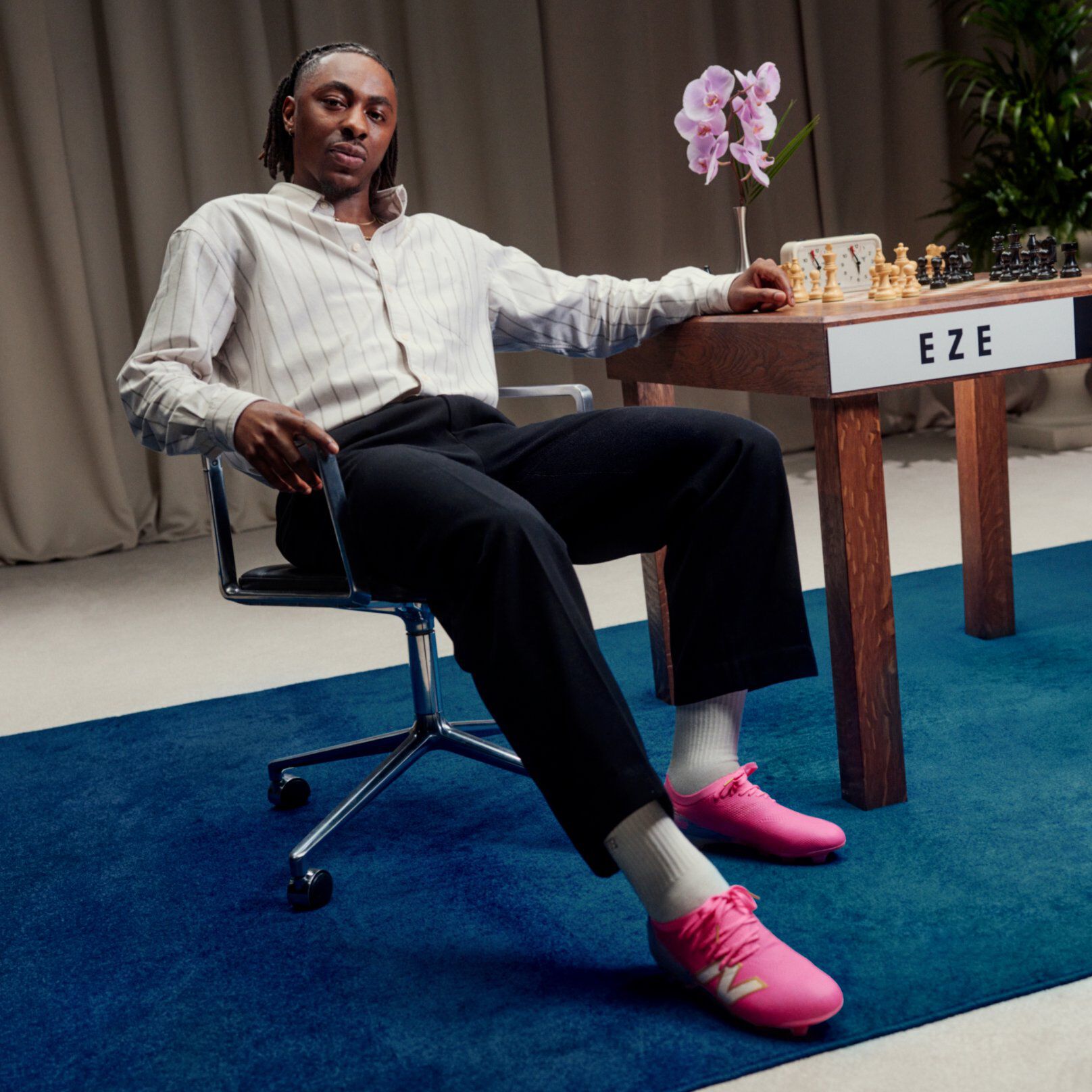 Eberechi Eze sitting in a chair beside a chess table, wearing bright pink New Balance sneakers.