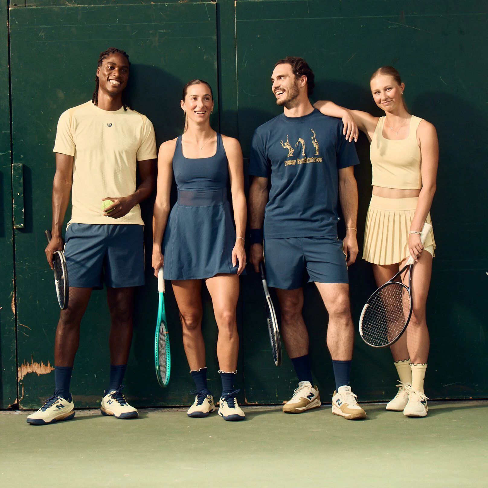 Four tennis players in coordinated athletic apparel stand against a dark green court wall holding rackets and a tennis ball.