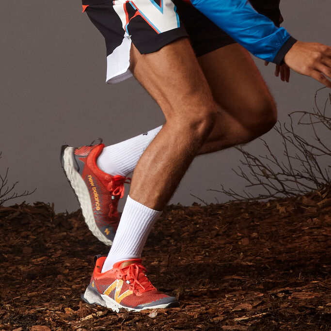 Male runner with bright orange trail shoes running on dirt and sticks. 