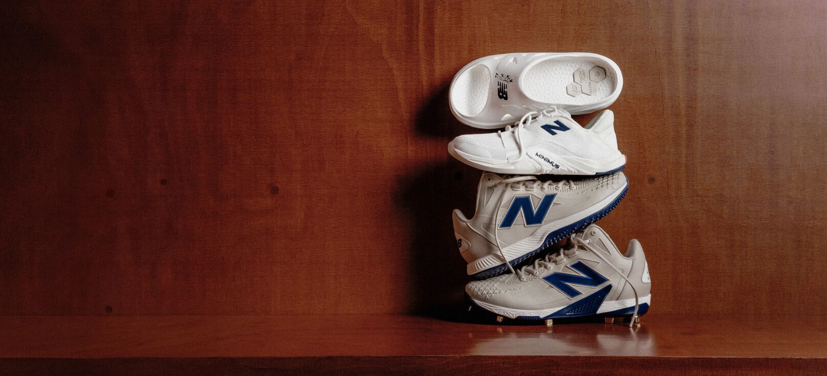Four different shoes and cleats sitting on top of each other on a wooden bench. 