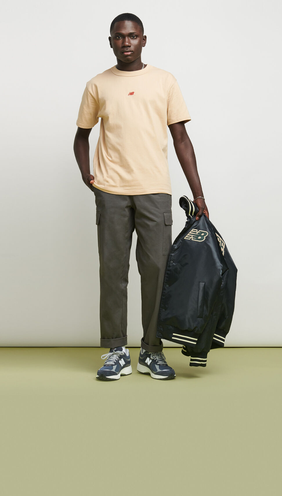 Joven africano con camiseta amarilla y chamarra en la mano sobre fondo gris. 