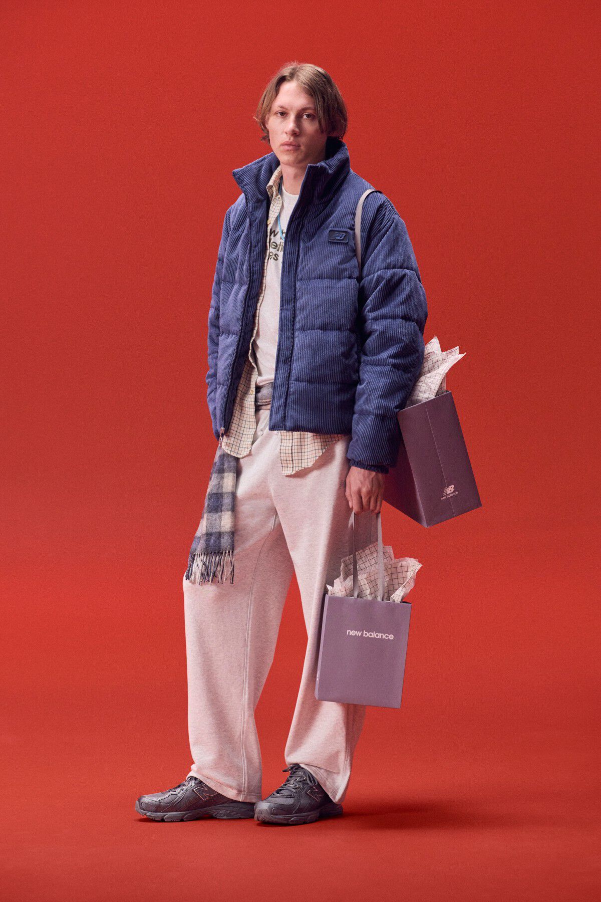 Joven con chaqueta azul que lleva una bolsa de regalos sobre un fondo rojo.