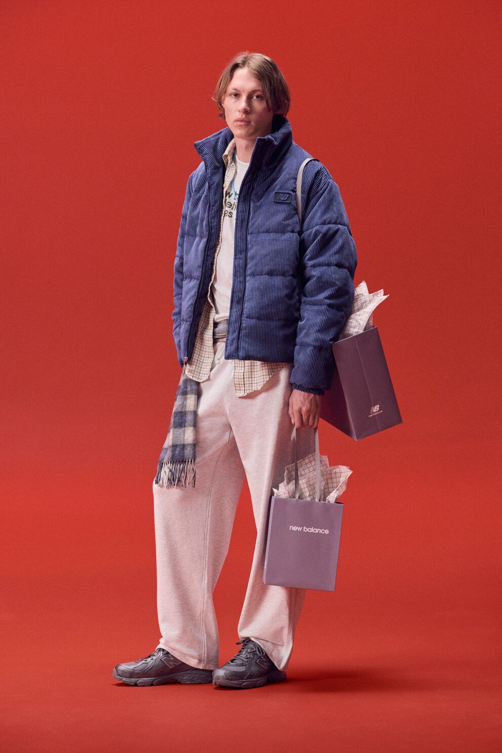 Joven con chaqueta azul que lleva una bolsa de regalos sobre un fondo rojo.