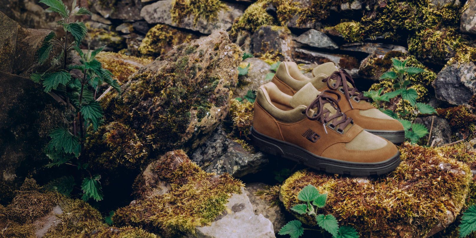 Un par de zapatillas New Balance Made in UK colocadas en un jard&iacute;n de rocas cubierto de musgo, rodeadas de peque&ntilde;as plantas verdes.