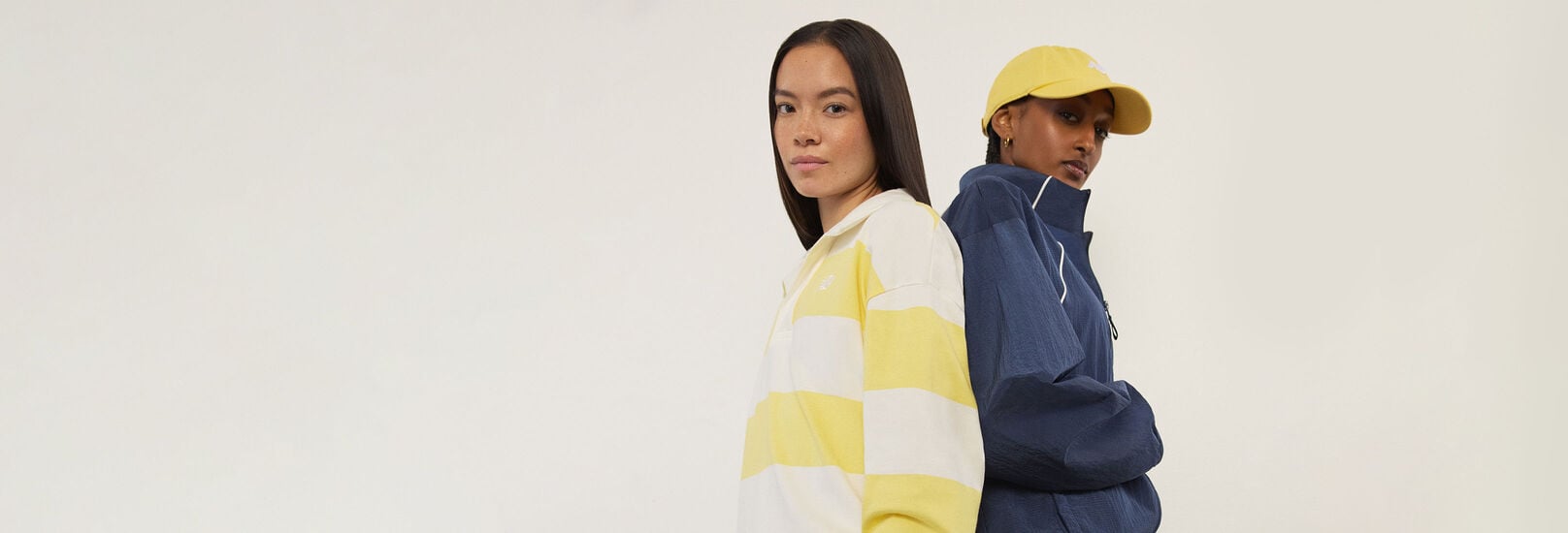 Two woman standing back to back and looking at the viewer.